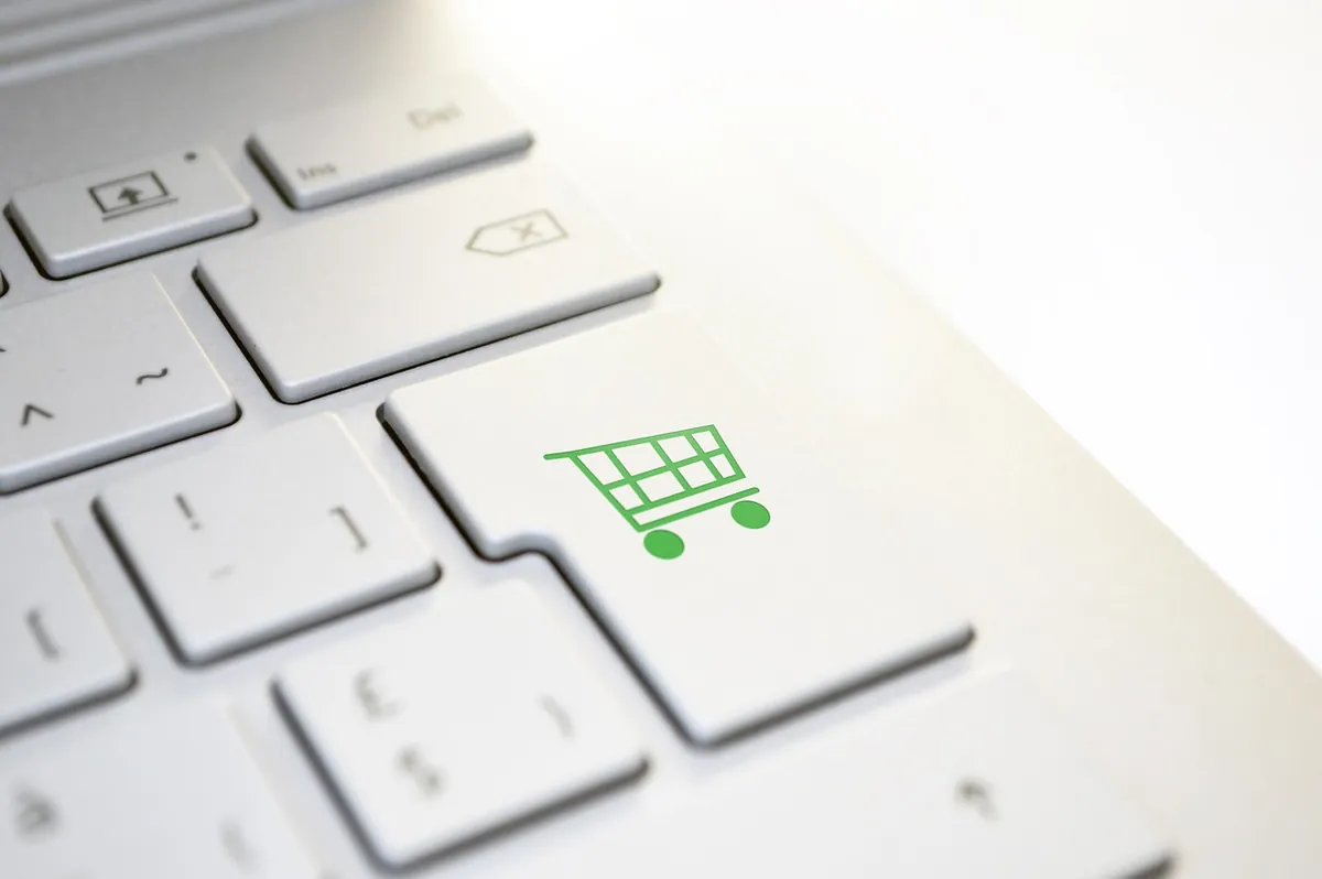 Close-up of a white laptop keyboard with a green shopping cart icon on the Enter key