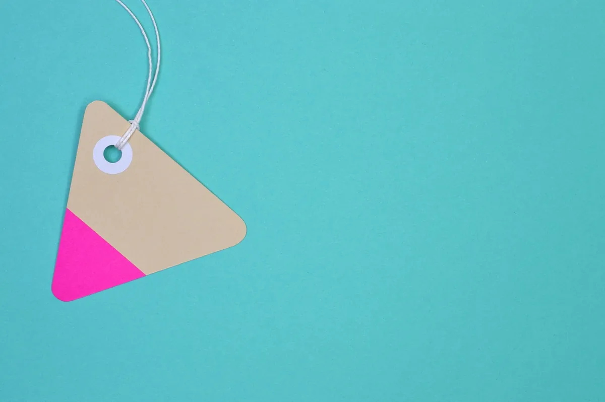 Blank triangular price tag on a string against a plain turquoise background