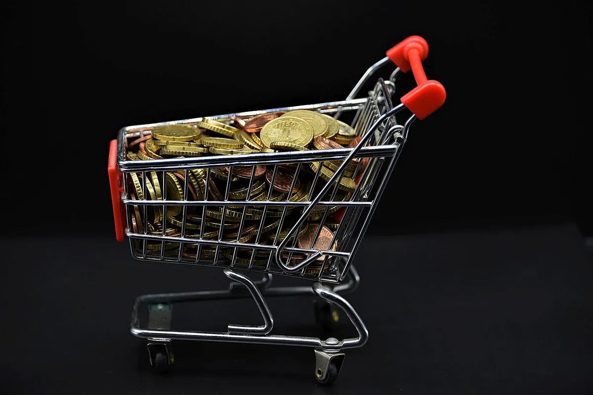 Small metal shopping cart filled with coins on a black background