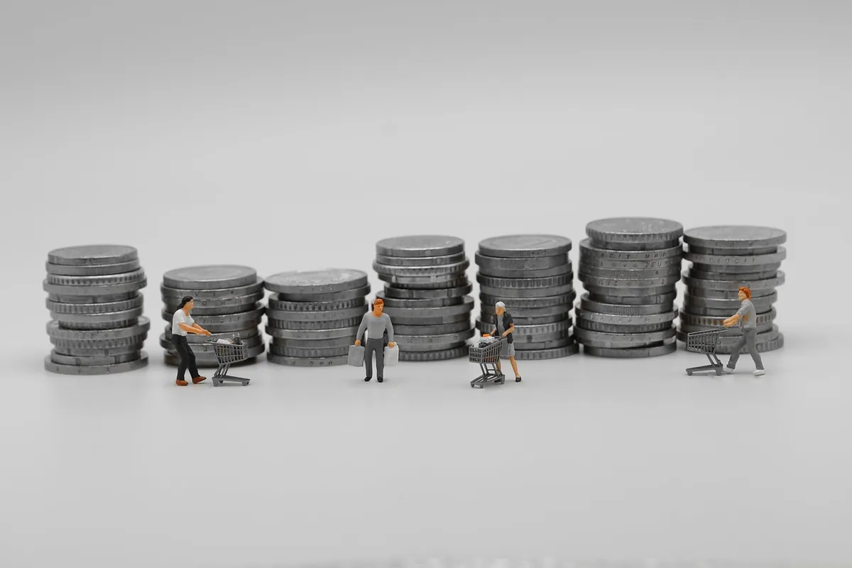 Miniature shoppers pushing carts in front of coin stacks of different heights